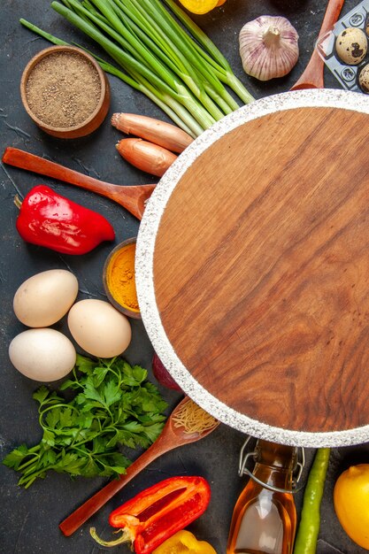 Above view of fresh vegetables fallen oil bottle salt pepper green bundle around cutting board on dark