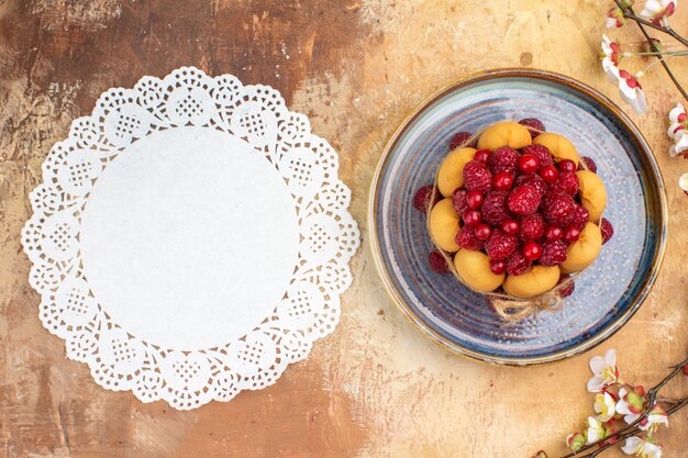 Above view of freshly baked soft cake with fruits flowers and napkin on mixed color table