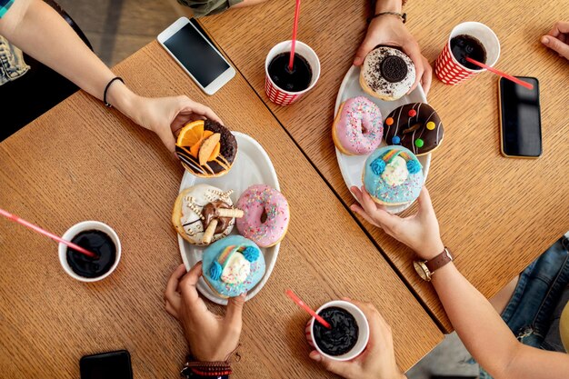 Above view of friends eating glazed donuts while gathering in a cafe