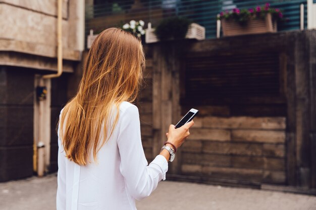 View from back of stylish woman with long blonde hair, using a mobile phone