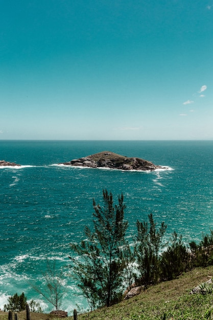 Foto gratuita vista da una scogliera che vede una piccola isola circondata dal mare su una scena di cielo limpido