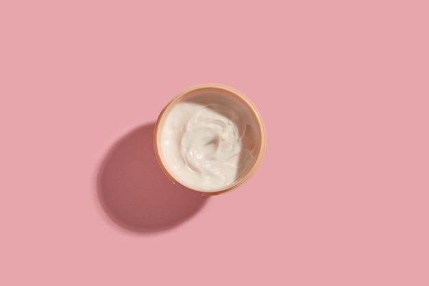 View from above to cream jar with white cream on pink background