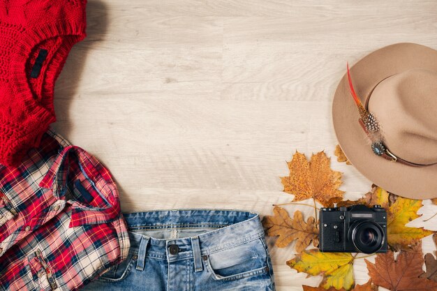 Вид сверху на плоскую планировку женского стиля и аксессуаров, красный вязаный свитер, клетчатую фланелевую рубашку, джинсовые джинсы, шляпу, осеннюю модную тенденцию, винтажную фотокамеру, костюм путешественника