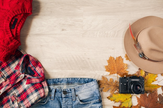 View from above on flat lay of woman style and accessories, red knitted sweater, checkered flannel shirt, denim jeans, hat, autumn fashion trend, vintage photo camera, traveler outfit