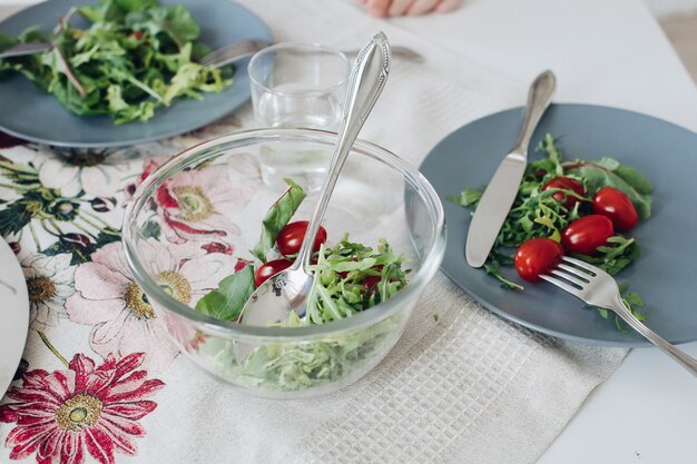 Вид сверху здоровых помидоров и зелени, лежащих на серой тарелке на кухне. Вкусные свежие овощи, нож и вилка, лежащие на столе в кафе. Понятие о кухне, диете и питании.