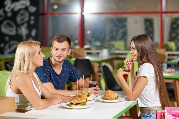 View from side of happy friends talking while eating in cafe