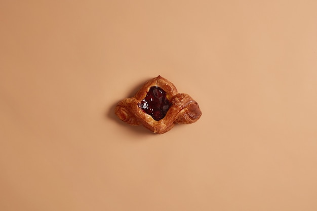 View from above of sweet crusty delicious bun filled with berry jam, baked at home, isolated over beige background. High sugar food and bakery products. Homemade pastry for your tasty breakfast