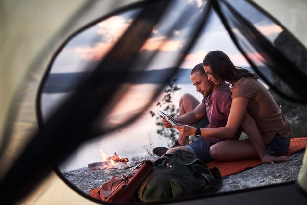 View from tent of couple with map lying a view of lake during hiking trip.