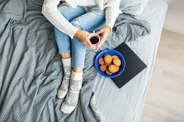 朝ベッドに座っている、カップでコーヒーを飲む、クッキーを食べる、朝食の女性の上からの眺め