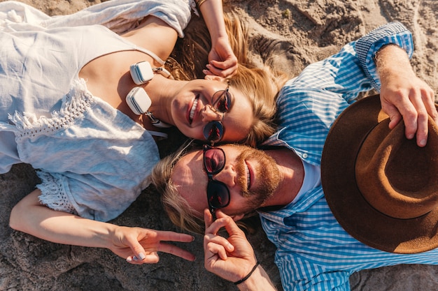 Foto gratuita vista dall'alto sul giovane sorridente felice uomo e donna in occhiali da sole sdraiato sulla spiaggia di sabbia