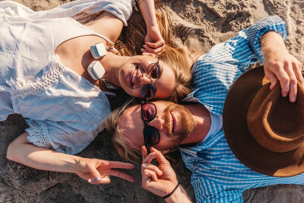 모래 해변에 누워 선글라스에 젊은 웃는 행복 한 남자와 여자에 위에서보기