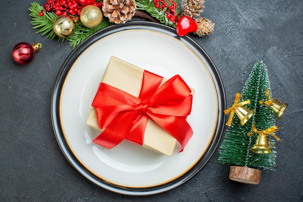 Above view of gift box on dinner plate christmas tree fir branches conifer cone on black background