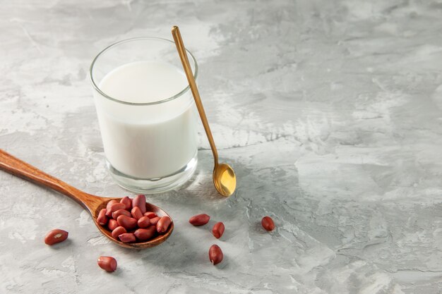 Above view of glass cup filled with milk and peanuts in spoon on gray background