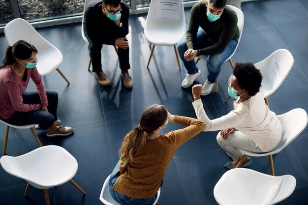 Above view of group therapy participants greeting with elbows due to coronavirus pandemic