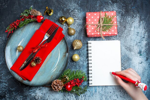 Above view of hand hlding a pen on spiral notebook and gift box next to cutlery set