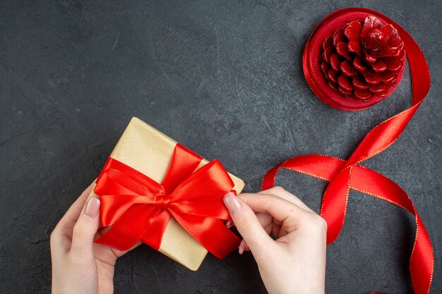 Above view of hand holding beautiful gift and conifer cone on dark background