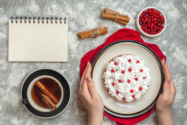 赤いタオルの上に果物で飾られたおいしいクリーミーなケーキを持っている手のビューの上