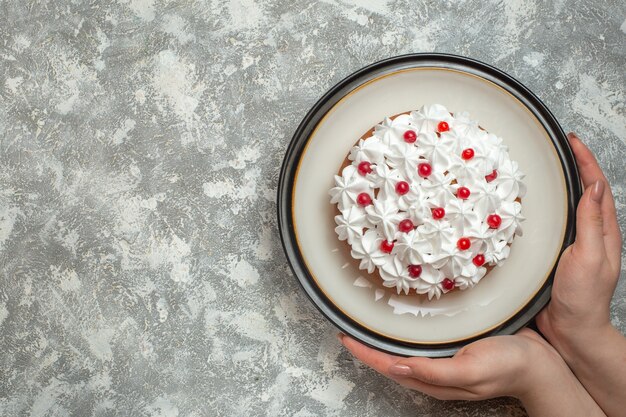 フルーツで飾られたおいしいクリーミーなケーキのプレートを持っている手のビューの上