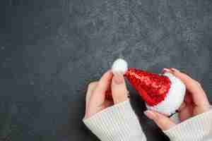 Free photo above view of hand holding santa claus hat on the left side on dark background