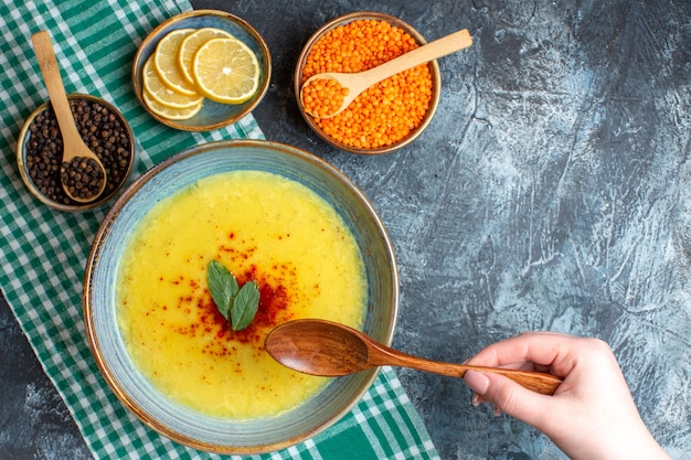 Above view of hand holding spoon tasty soup served with mint and pepper on a green stripped towel