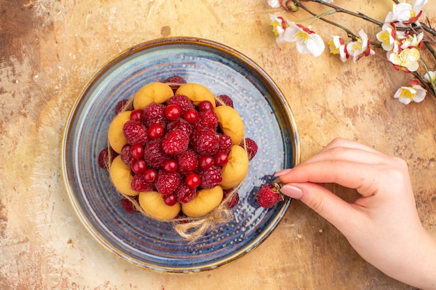 혼합 색상 테이블에 과일과 함께 갓 구운 부드러운 케이크에 딸기를 들고 손의보기 위