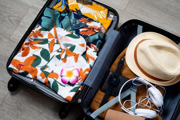 View of hawaiian shirts stacked in luggage with hat and headphones