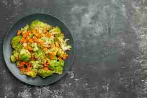 Foto gratuita sopra la vista del pasto sano con broccoli e carote su un piatto nero sul tavolo grigio