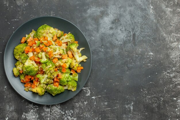 Выше вид здоровой еды с брокколи и морковью на черной тарелке на сером столе