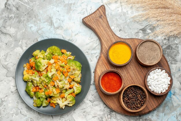 Above view of healthy vegetable salad different spices and cutting board on white table