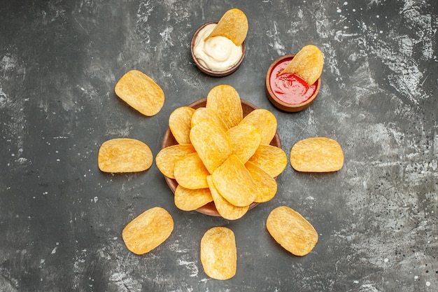 Above view of homemade potato chips arranged in a circle and mayonnaise ketchup on gray table