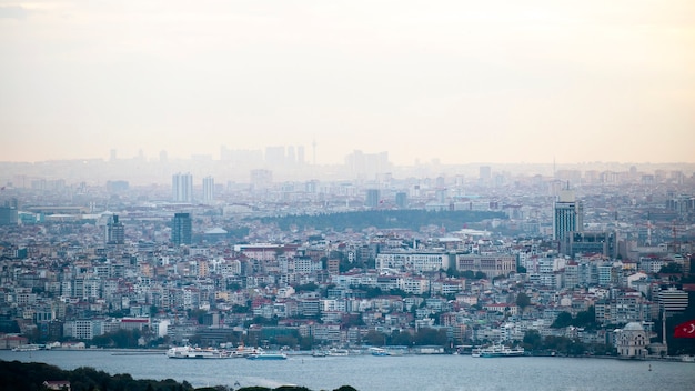 Вид на Стамбул в пасмурную погоду, несколько низких и высоких зданий, туман, пролив Босфор на переднем плане, Турция