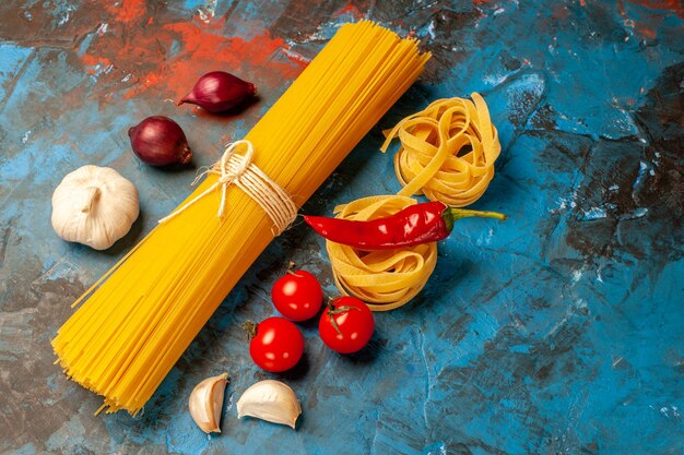 Above view of Italian various pastas for dinner preparation garlics peppers tomatoes onions on blue background