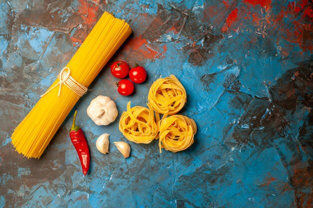 Above view of Italian various pastas for dinner preparation garlics peppers tomatoes onions on the right side on blue background