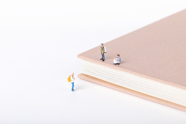 View of little figurines of students standing onnd around a textbook on white