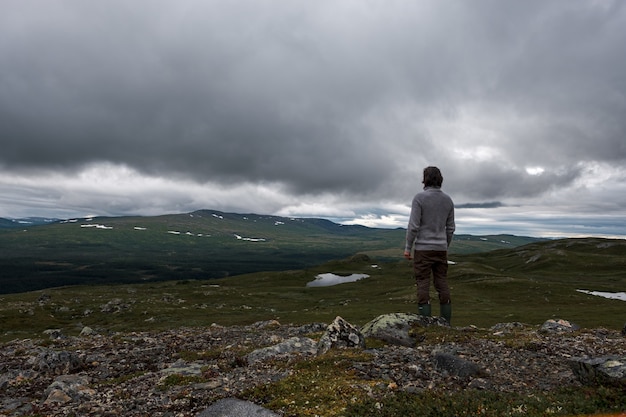 View of a man standing on a rocky hill with a stormy clouds