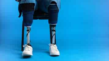 Free photo view of a man with prosthetic legs and white sneakers sitting on a chair blue background