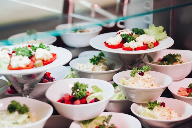 Вид на множество круглых тарелок с вкусными овощами, блюдо из салатов с помидорами, луком, цуккини, помидорами и зеленью. Большой вкусный ужин в ресторане