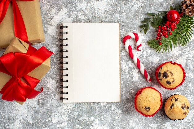 Above view of notebook and small cupcakes candy and fir branches decoration accessories and gift with red ribbon on ice surface