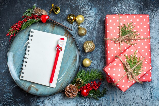 Above view of notebook with pen on blue plate decorative accessories and a gift box on dark background