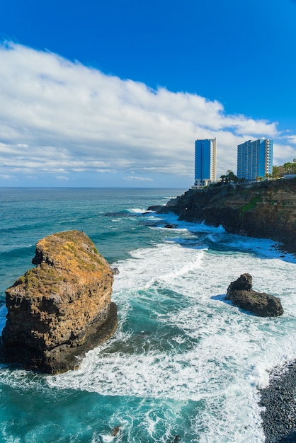 プンタブラバ、プエルトデラクルーズ、テネリフェ島、カナリア諸島、スペインの岩の上の海の海岸とホテルの建物を見る