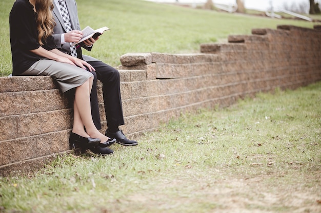 Бесплатное фото Вид пары в строгой одежде и чтения книги, сидя в саду
