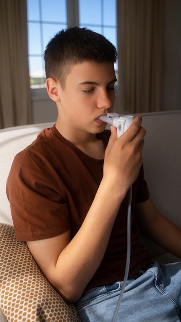 無料写真 呼吸器系の健康上の問題のために自宅で吸入器を使用している十代の少年の様子