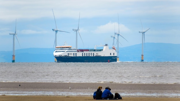英国の海岸線の眺めビーチの風車と遠くの船に乗っている人々のグループ