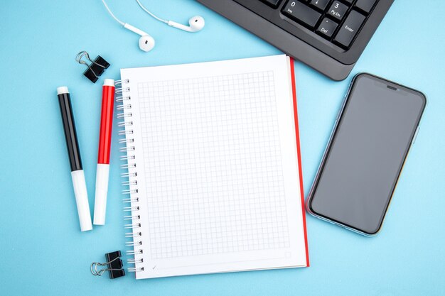 Above view of office concept with mobile phone headphone and spiral notebook on blue surface