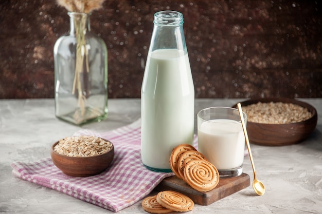 Sopra la vista della bottiglia di vetro aperta e della tazza riempita di avena di biscotti al latte in vaso marrone su asciugamano spogliato viola su tagliere di legno