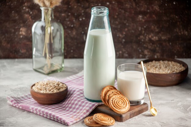 above view of open glass bottle and cup filled with milk cookies oats in brown pot on purple stripped towel on wooden cutting board