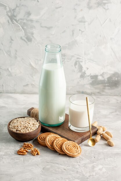 Above view of open glass bottle cup filled with milk spoon and walnut oats in brown pot cookies on ice background