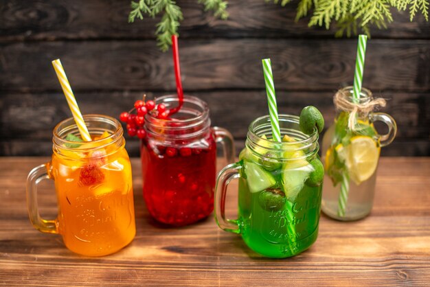 Above view of organic fresh juices in bottles served with tubes and fruits on a brown wooden background