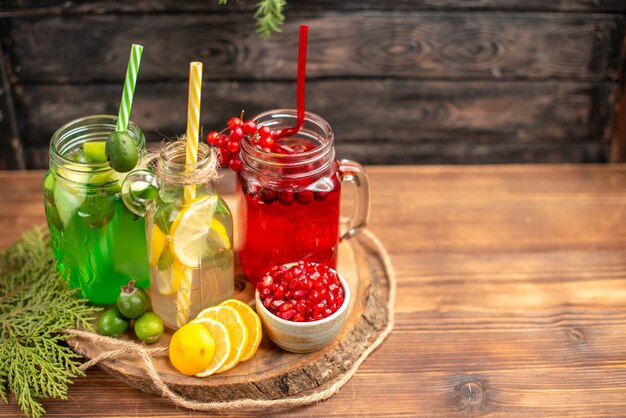 Above view of organic fresh juices in bottles served with tubes and fruits on a wooden cutting board