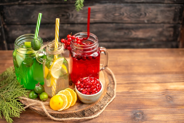 Above view of organic fresh juices in bottles served with tubes and fruits on a wooden cutting board